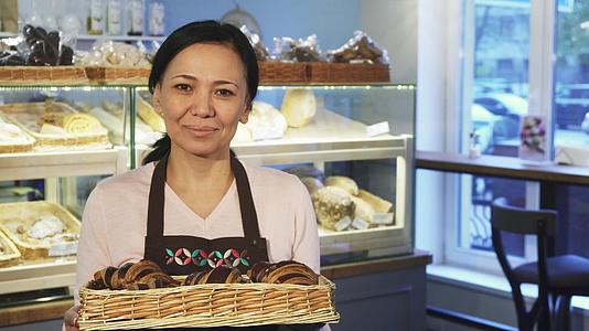 成熟的女面包师在她的店里摆满了一篮子羊角面包视频的预览图