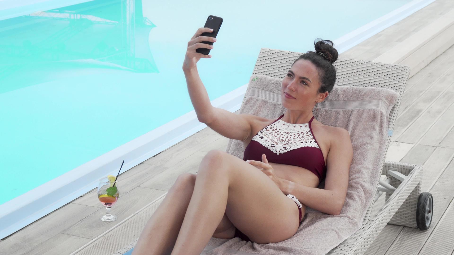 漂亮的女士用智能手机在游泳池边休息时用智能手机自拍视频的预览图