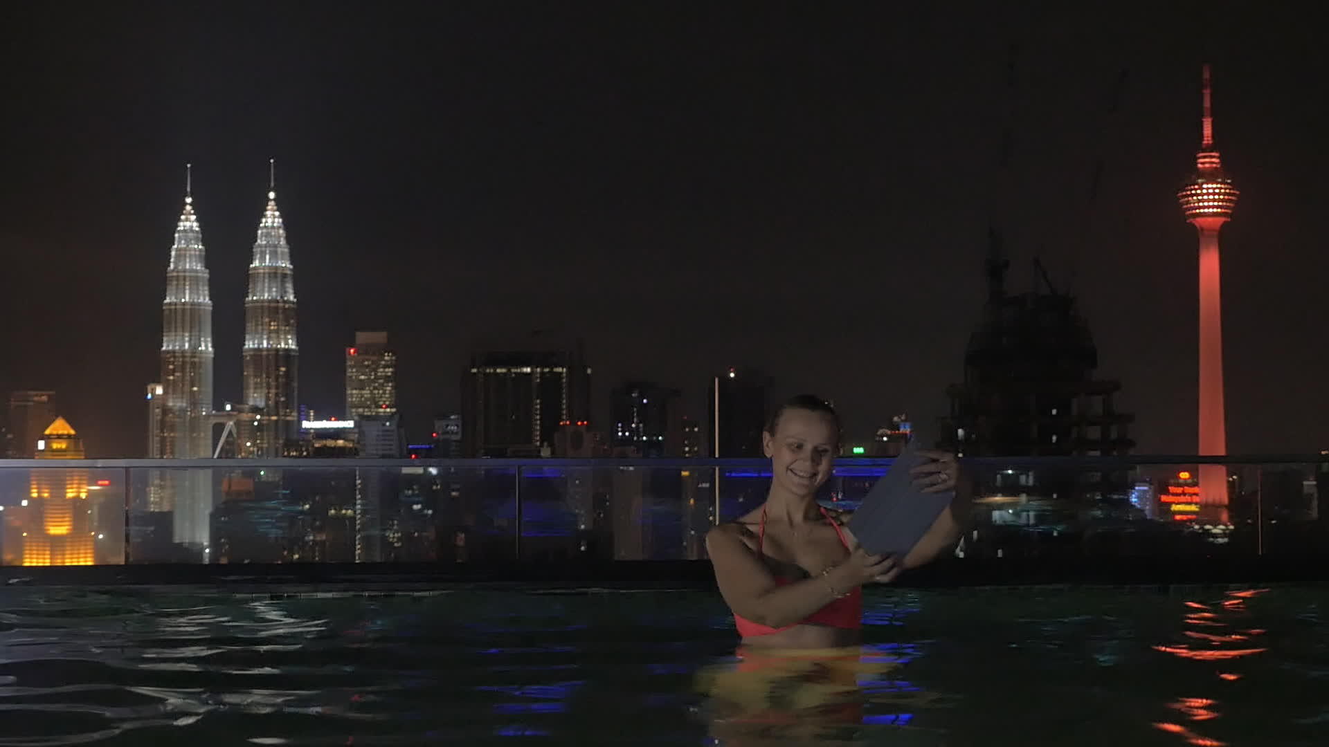 在摩天大楼屋顶上的游泳池里女性用平板自拍晚上在城市里自拍视频的预览图