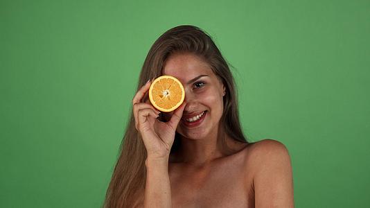 一个美丽快乐的女人的工作室微笑着拿着半个橘子视频的预览图