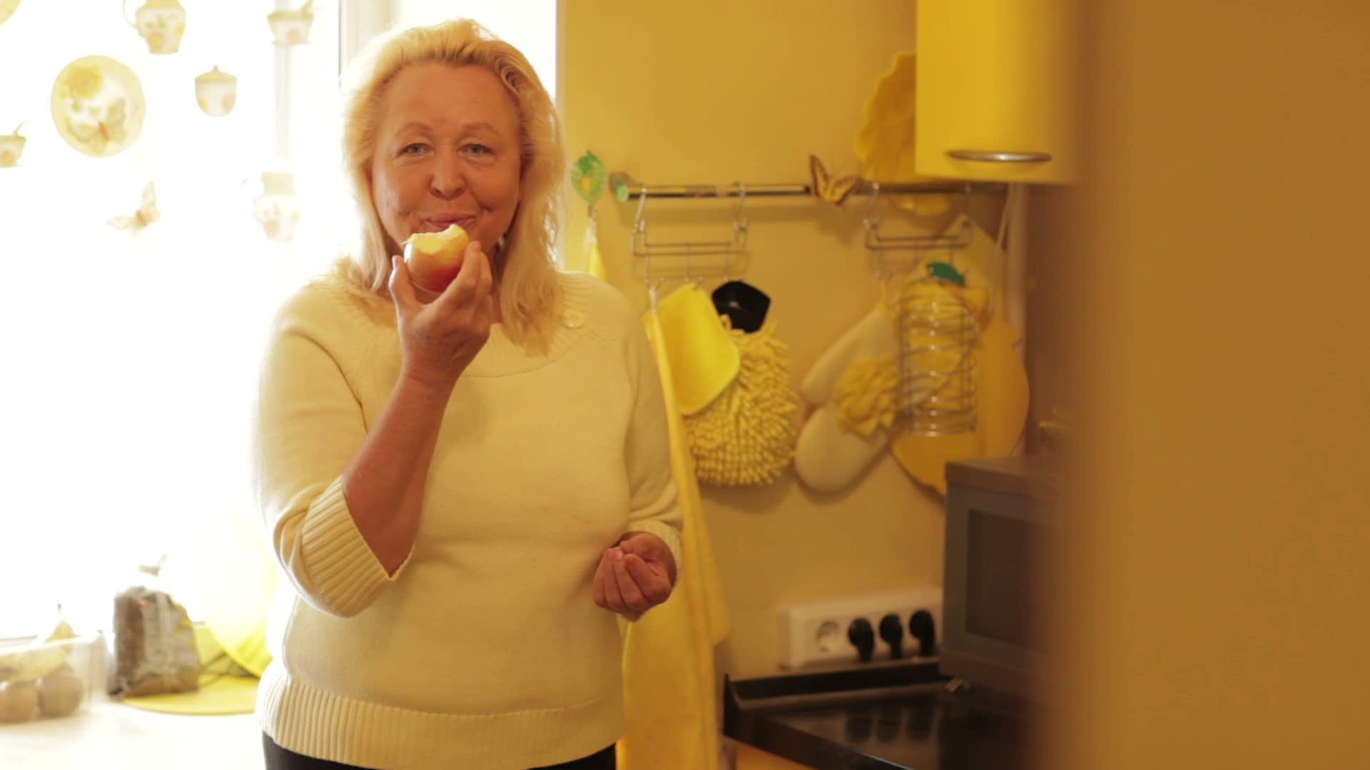 在黄色厨房吃苹果的老妇人视频的预览图