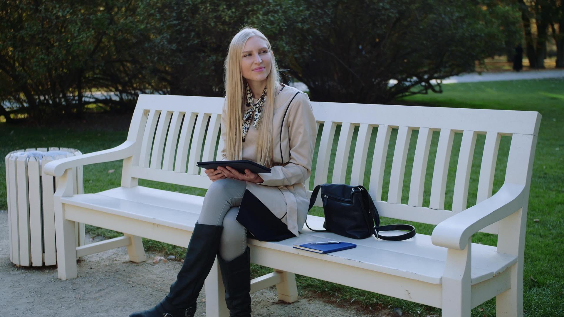 坐在秋天公园长椅上的年轻美女在平板板上工作视频的预览图
