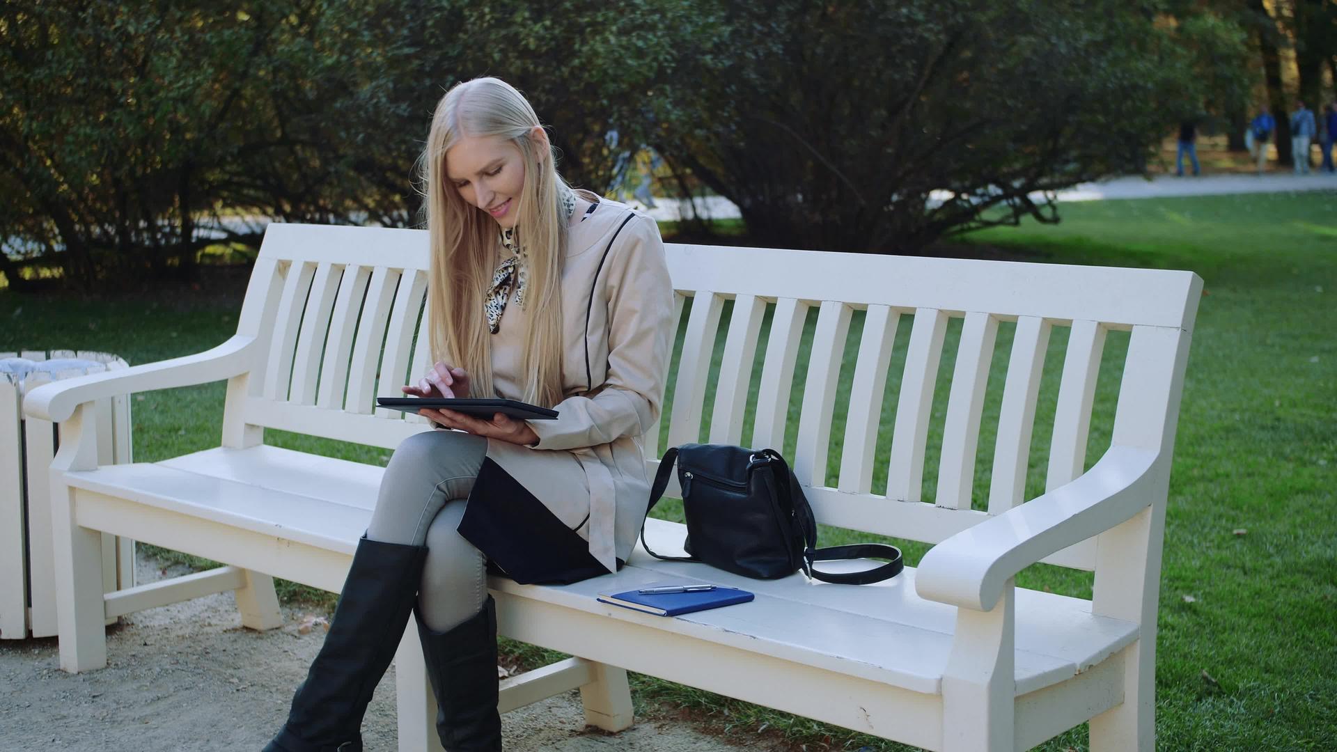 公园里有平板电脑的快乐女孩在秋季公园的长椅上视频的预览图