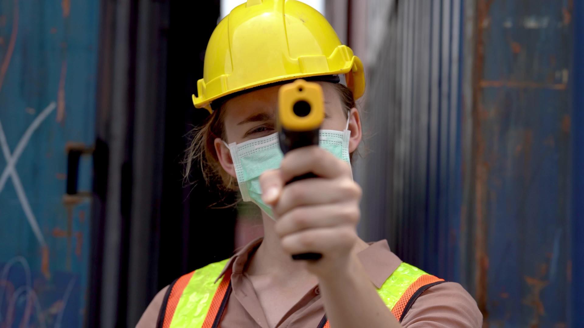戴口罩的女工用非接触式红外温度计测量温度并举手取消视频的预览图