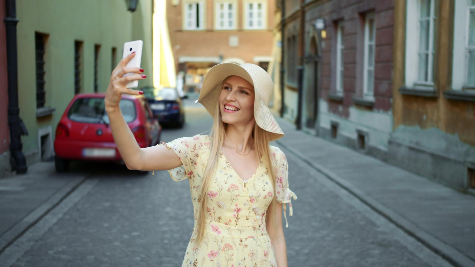 快乐的年轻女孩走在旧欧洲的街道上用智能手机自拍视频的预览图