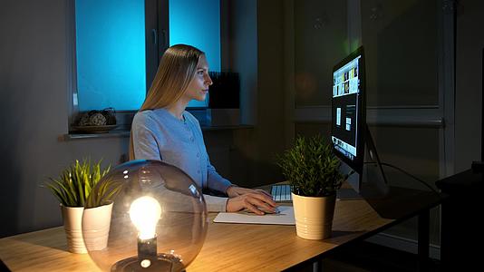 晚上女性专注于看电脑穿着温暖的家居服轻松美丽的金发视频的预览图
