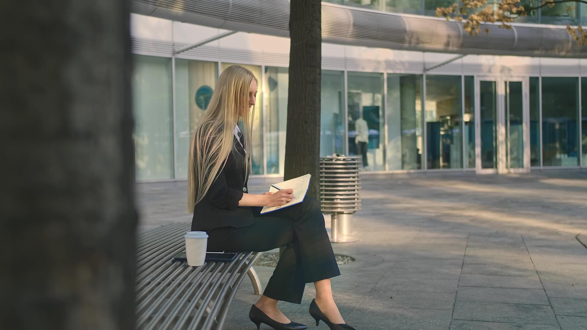 成功的年轻女性在户外做笔记优雅的女商人坐在院子里的长椅上视频的预览图