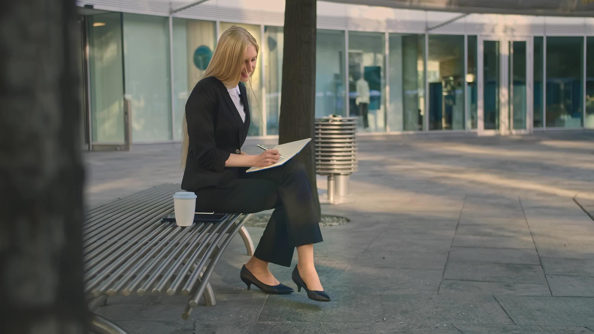成功的商业女性在户外做笔记优雅的女孩坐在院子里的长椅上视频的预览图