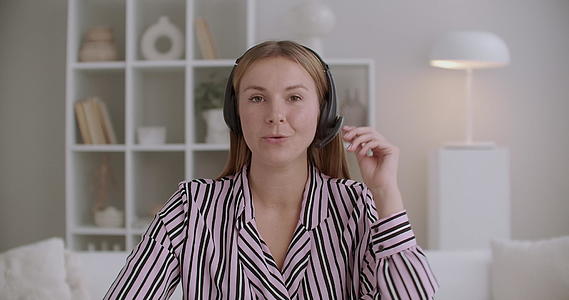 友好的年轻女性用麦克风在镜头上用耳机说话视频的预览图