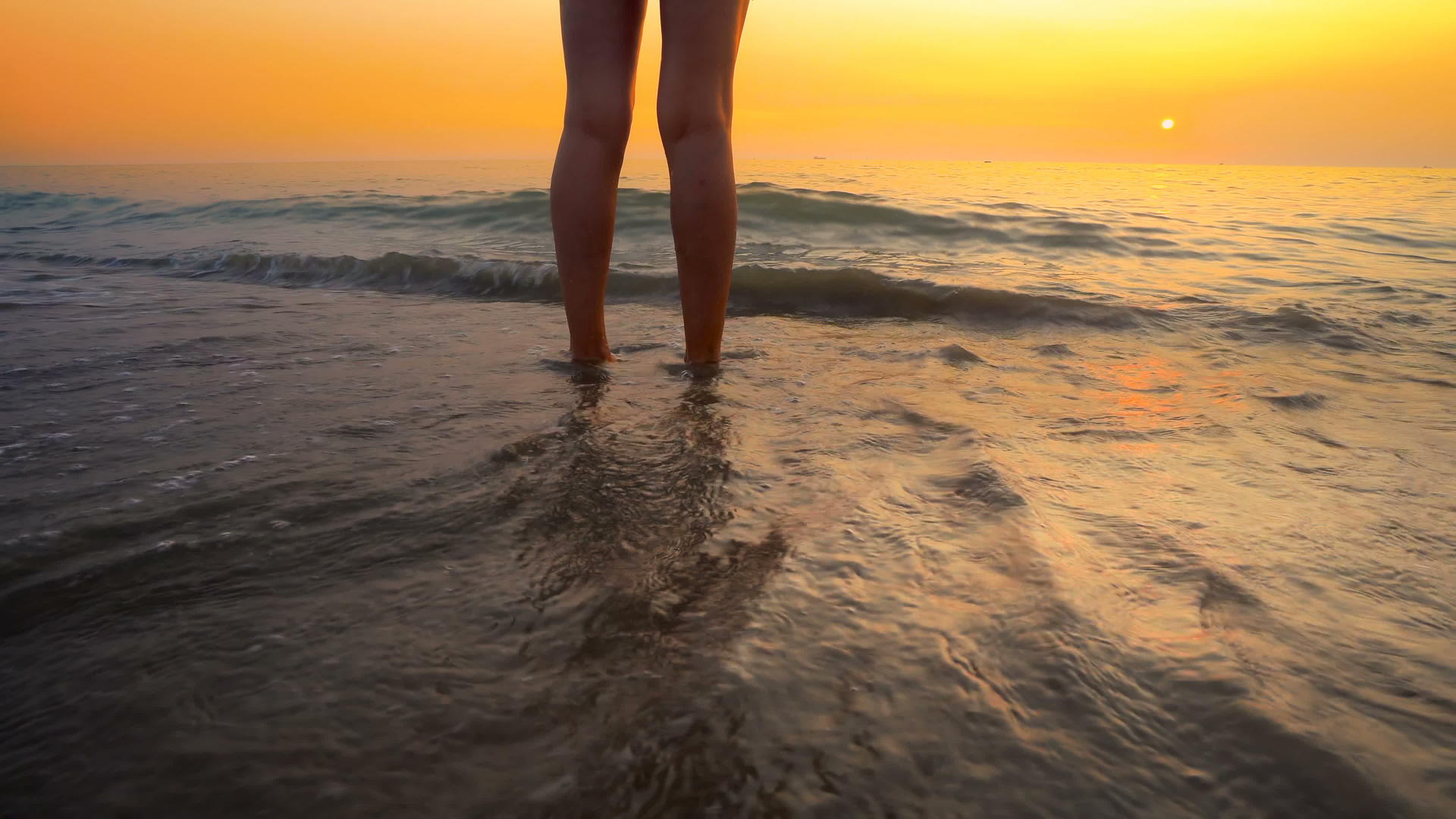 当海滩日落时女人的脚被海浪溅在美丽的海滩上视频的预览图
