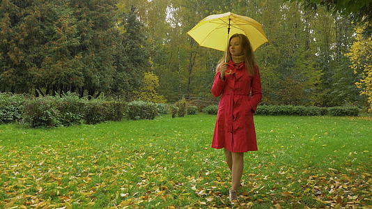 下雨天穿着红色斗篷和黄色雨伞的苗条年轻女子正在走路视频的预览图