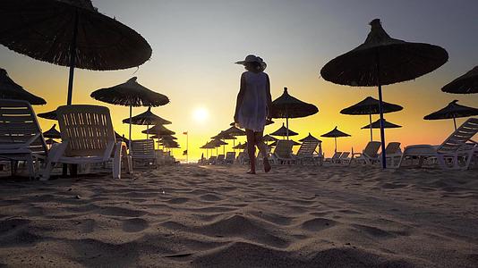 穿着白色连衣裙和帽子的妇女在海边度假胜地的海滩上散步视频的预览图