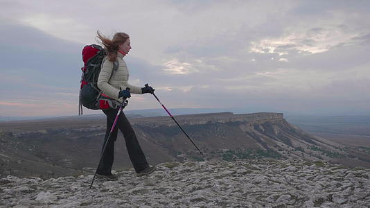 年轻的登山女孩带着背包和步行杆在岩石边缘行走视频的预览图