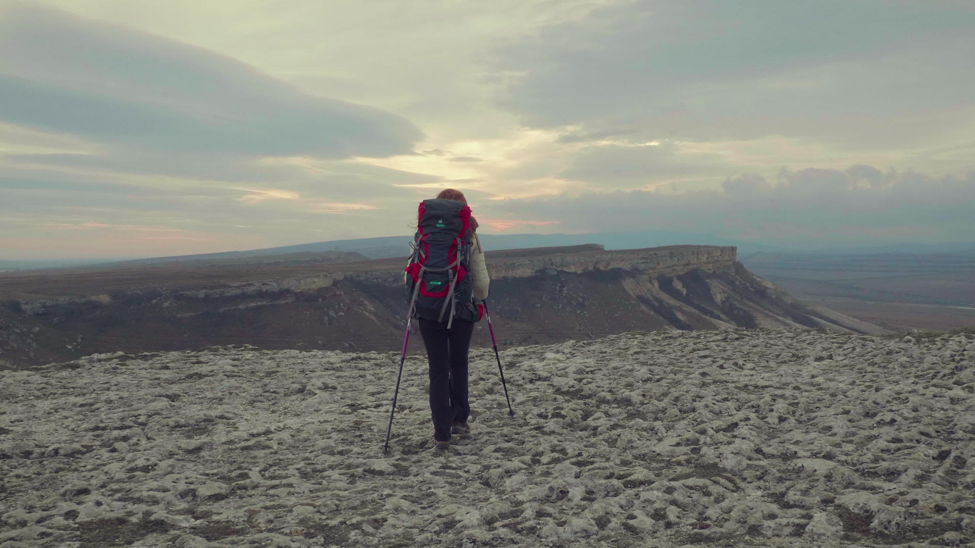 年轻的登山女孩站在岩石边缘带着背包和徒步杆稳定地站在岩石边缘视频的预览图