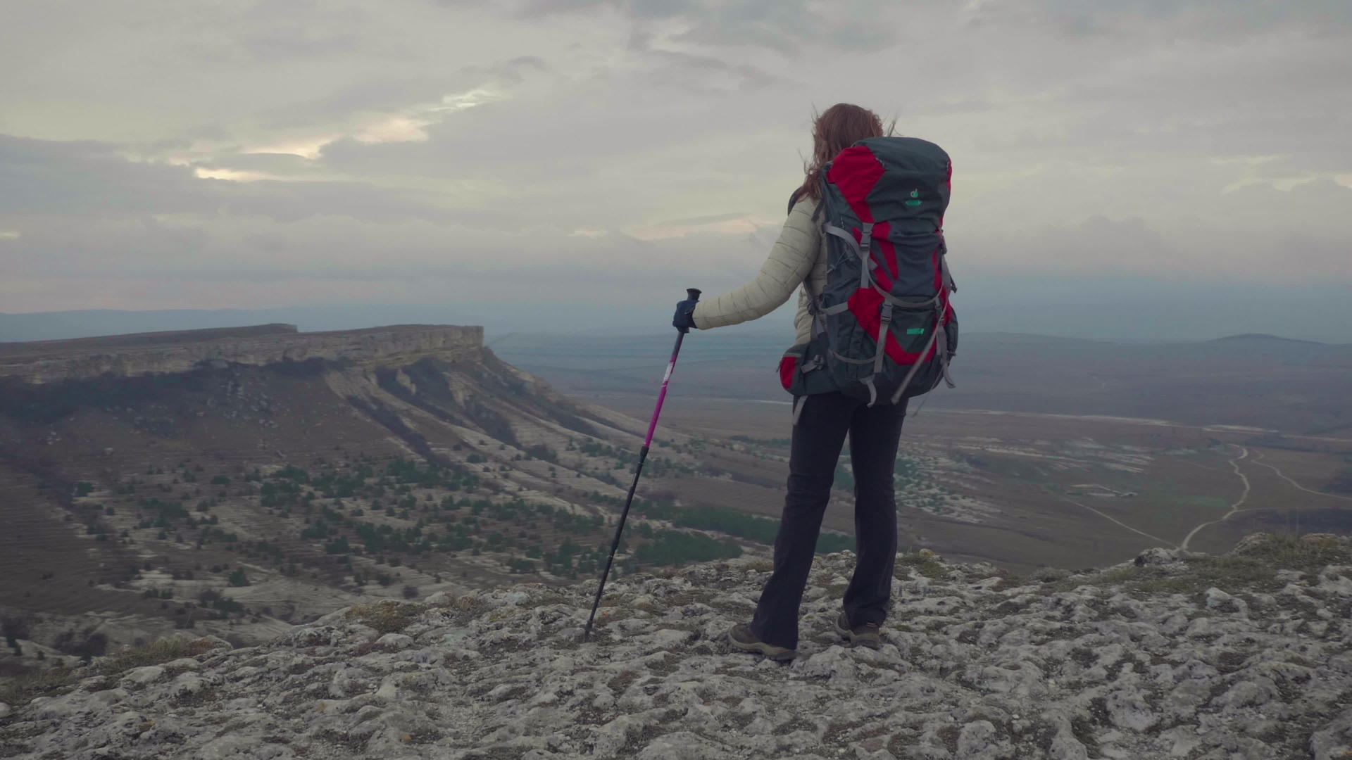 年轻的登山女孩站在岩石边缘背着背包和徒步杆视频的预览图