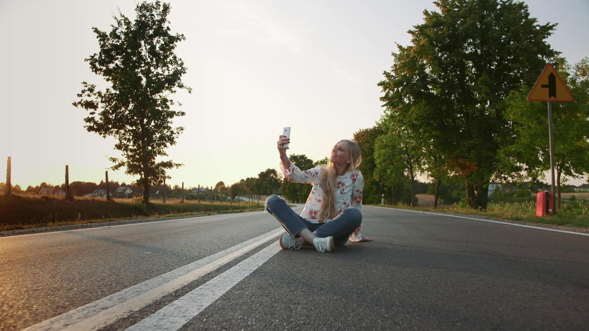 可爱的年轻女士坐在欧洲乡村的路上在路上自拍视频的预览图