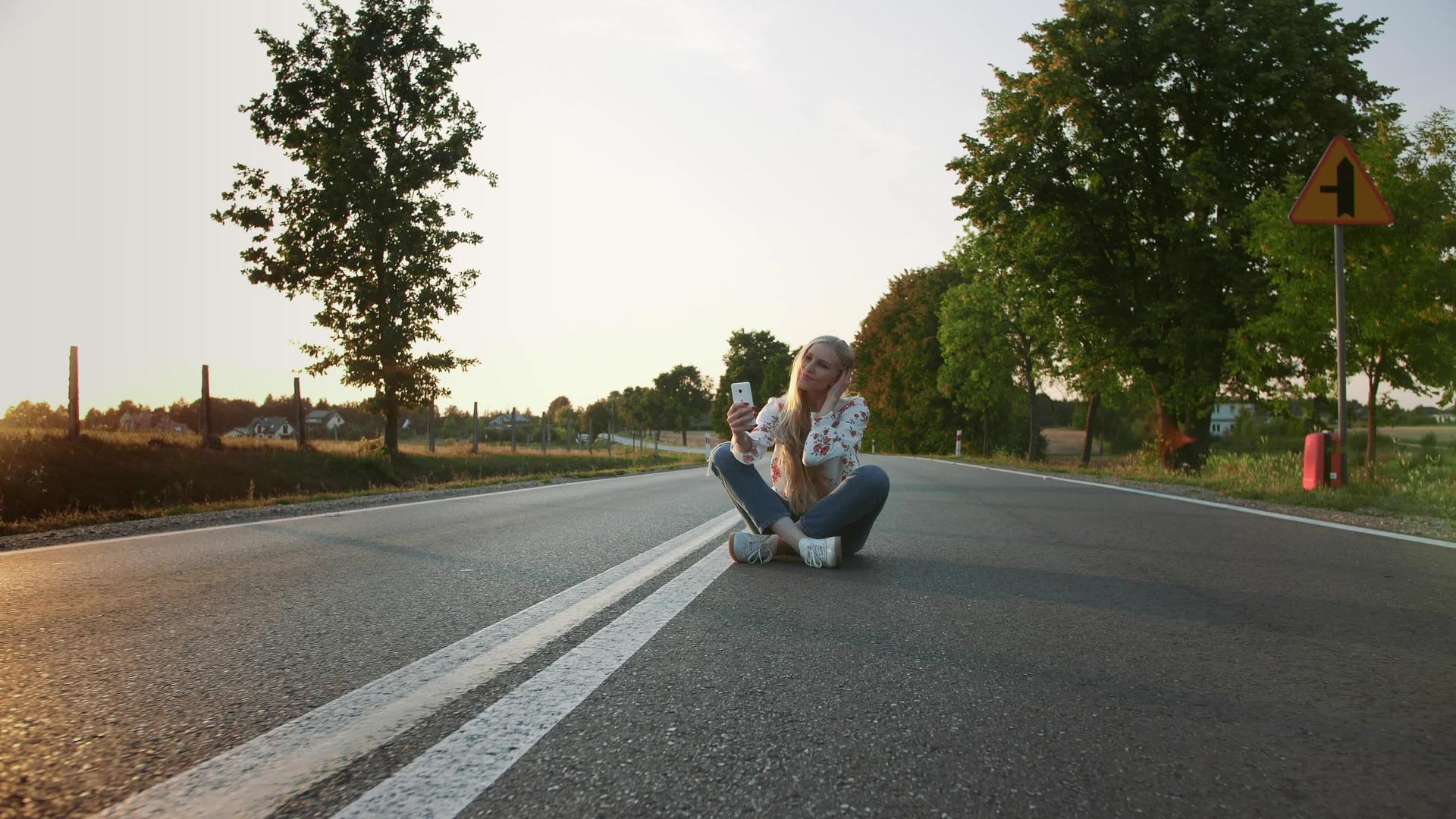 可爱的年轻女士坐在欧洲乡村的路上在路上自拍视频的预览图