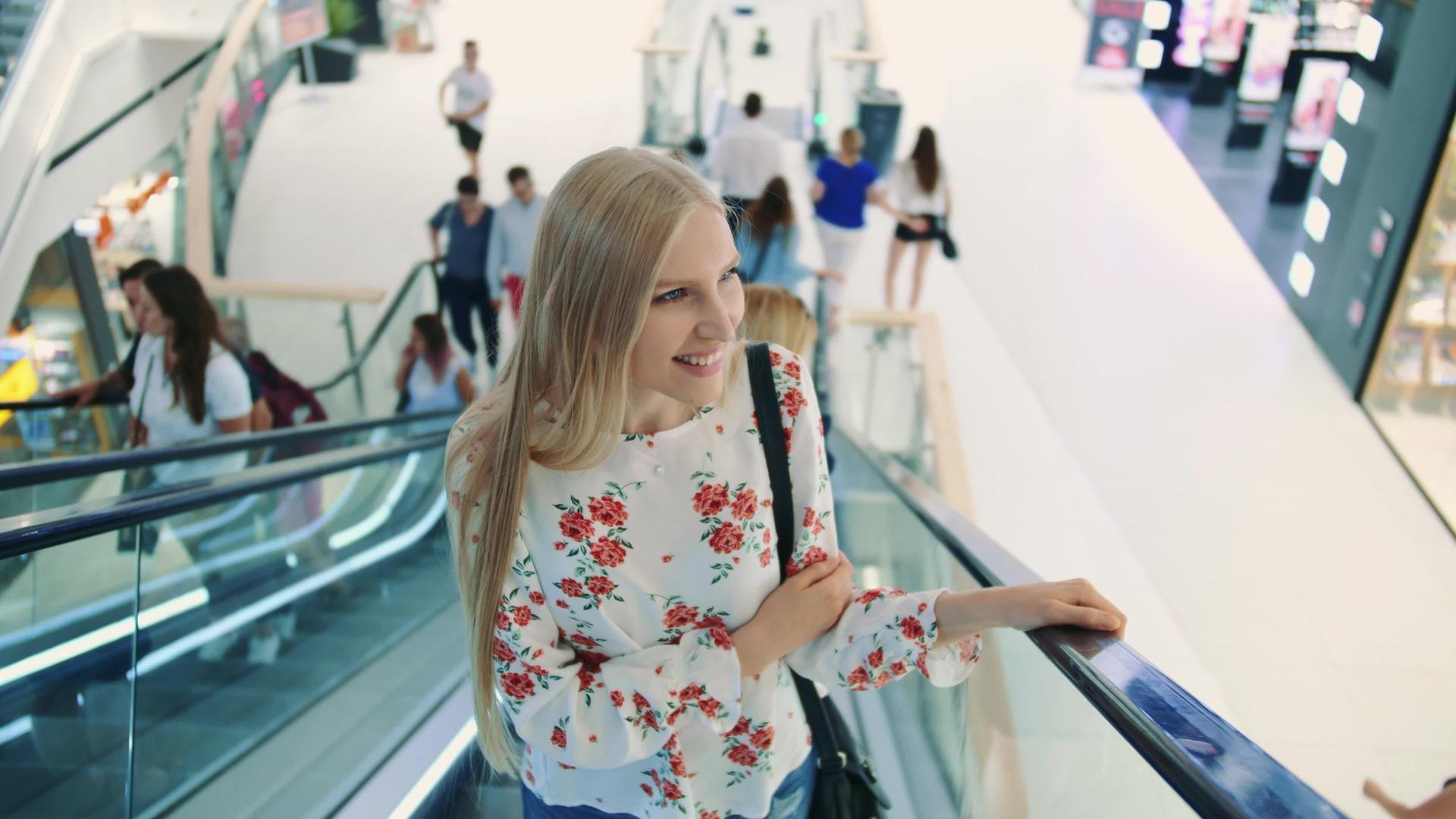 年轻的金发女人骑在自动扶梯上的购物中心视频的预览图