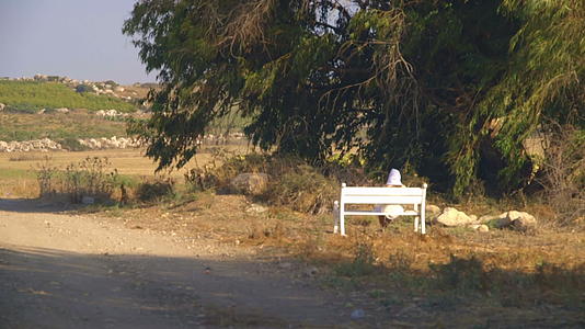 金发女人穿着白色的裙子白色头巾坐在长凳上视频的预览图