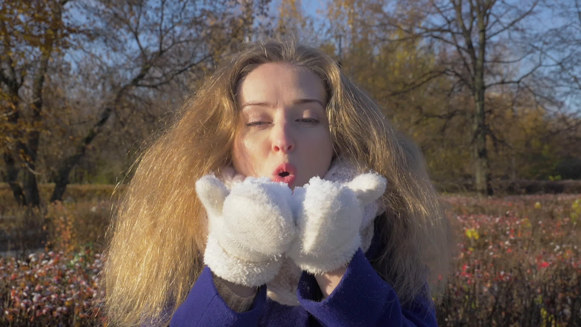 穿着白手套的年轻美女在阳光明媚的冬季公园里吹雪视频的预览图