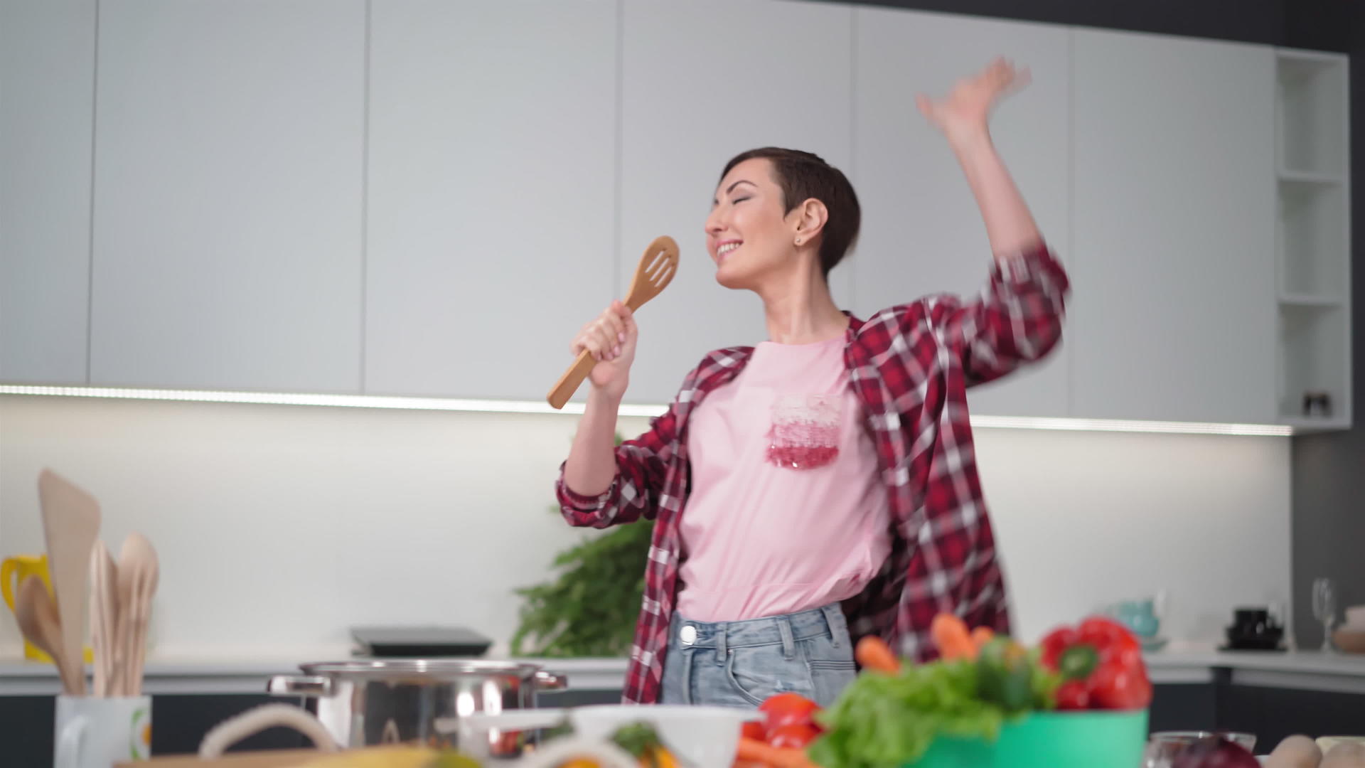 年轻快乐的女人用麦克风跳舞用木勺在新家厨房准备食物视频的预览图