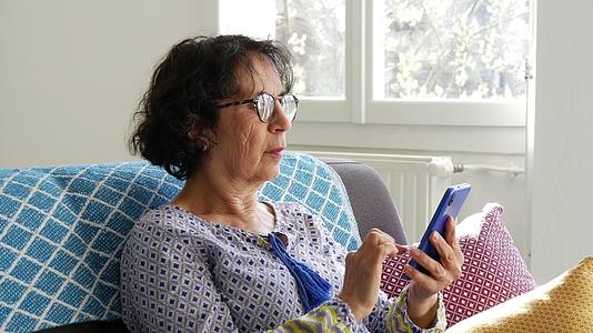 老妇人用智能手机坐在沙发上视频的预览图