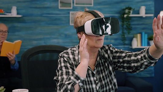 退休中老年妇女在客厅使用虚拟现实护目镜视频的预览图