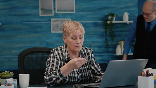 高级女性使用笔记本电脑信用卡在线支付视频的预览图