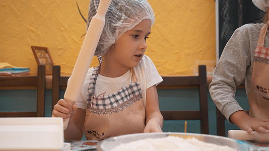 一次性帽子的小女孩和女厨师在学校厨房准备面团视频的预览图
