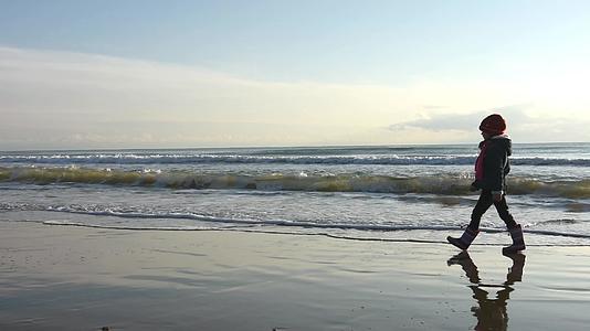 一个五岁的女孩在秋天的靴子上沿着海滩散步视频的预览图