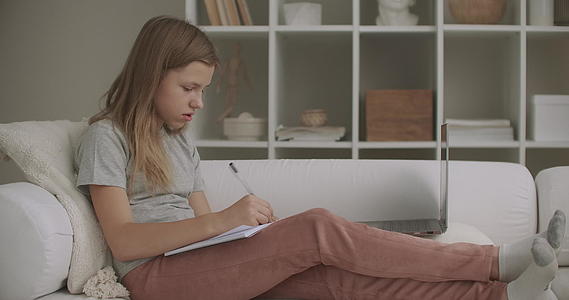 青少年女孩在书上写字周末她们坐在家里的客厅沙发上视频的预览图