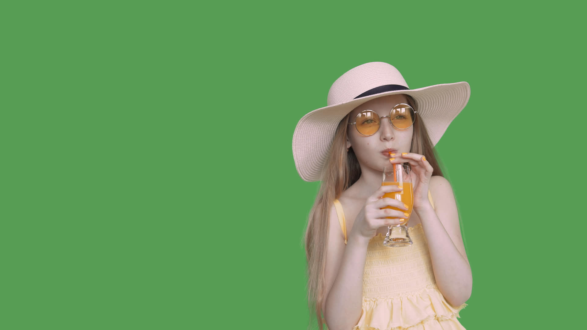 戴着黄色眼镜和帽子的年轻女孩在绿屏上喝果汁视频的预览图