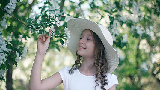 浪漫的女孩在盛开的果园里嗅着苹果树的花朵春天她戴着白色的视频的预览图