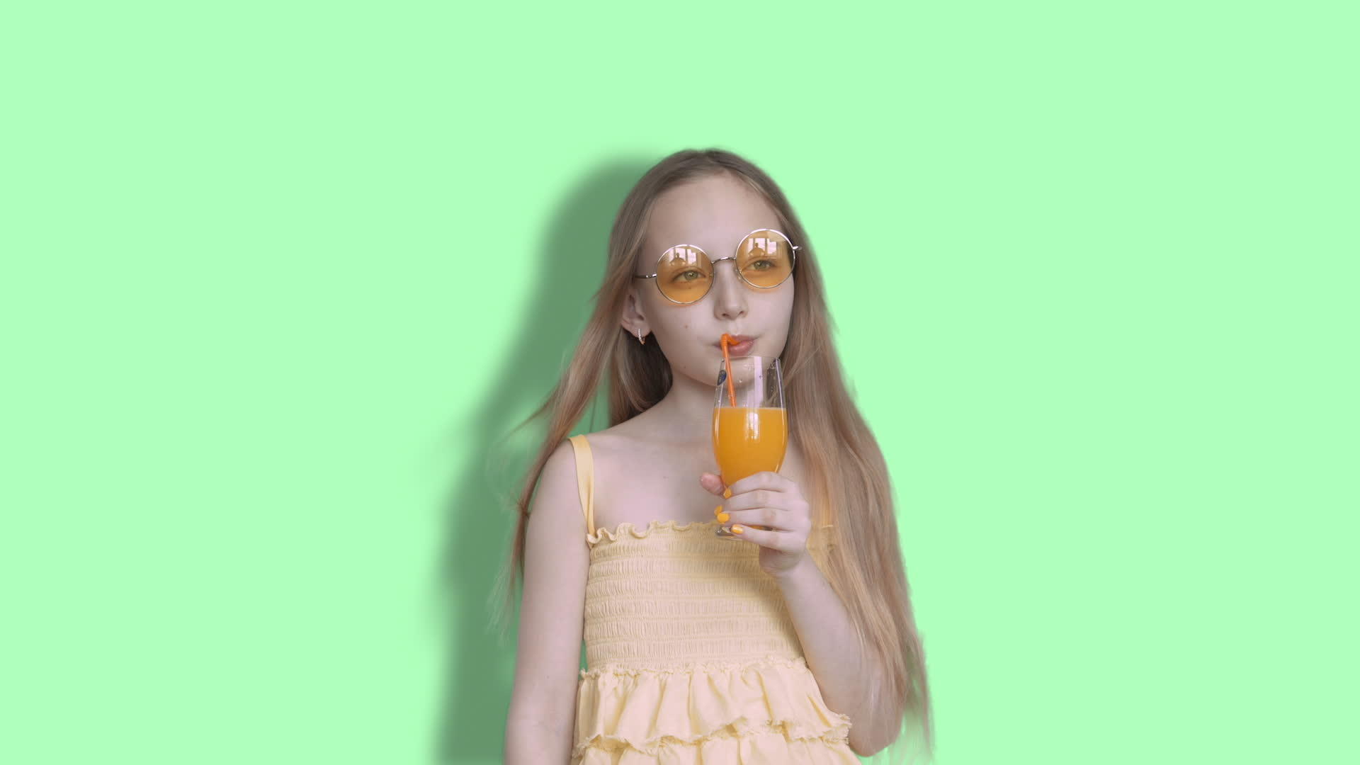 一个戴着黄色太阳镜的女孩在工作室的背景下喝水果鸡尾酒Chocking视频的预览图