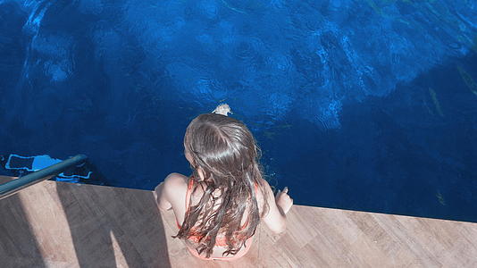 坐在游泳池边的女孩的腿在游泳池外面的头顶视图视频的预览图