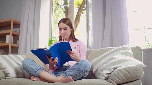 年轻女士坐在沙发上看杂志视频的预览图