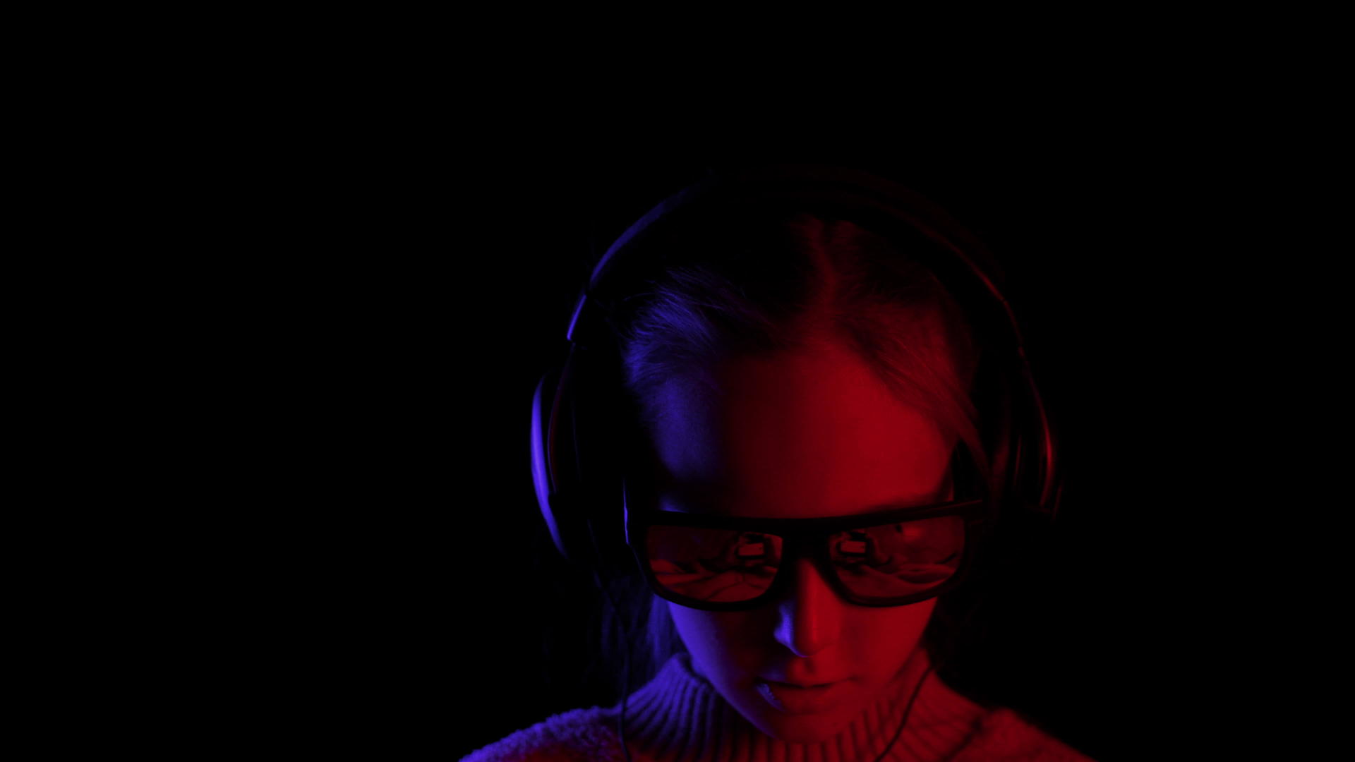 女孩在黑暗中用太阳镜和耳机浏览电话视频的预览图