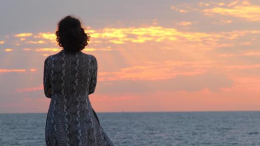 穿着夏装的年轻女子在日出和海景的背景下看着大海视频的预览图