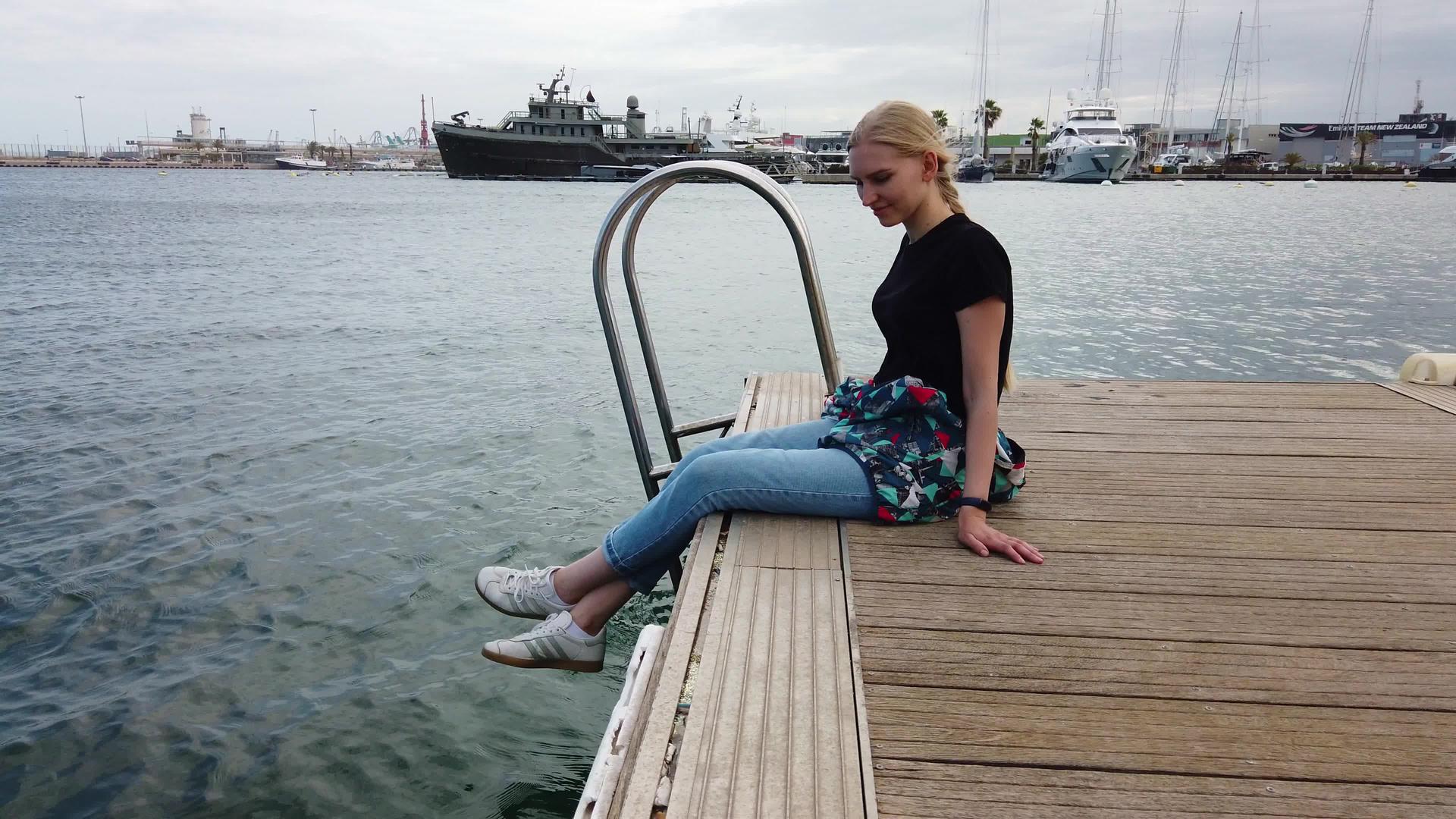 美丽的女孩坐在停泊在度假镇港口的船上视频的预览图
