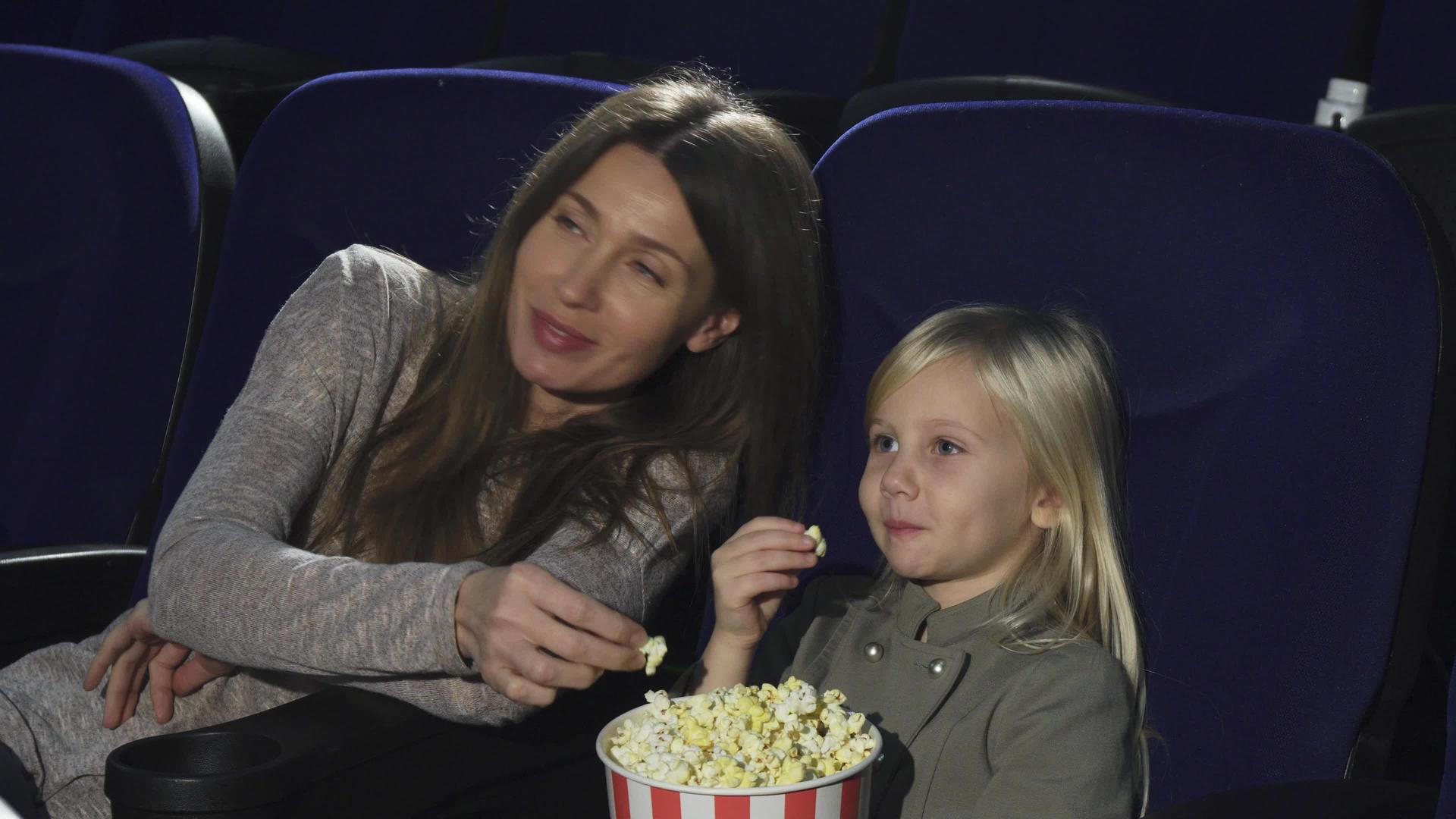 美丽的女人和她的小女儿在电影院吃爆米花和看电影视频的预览图