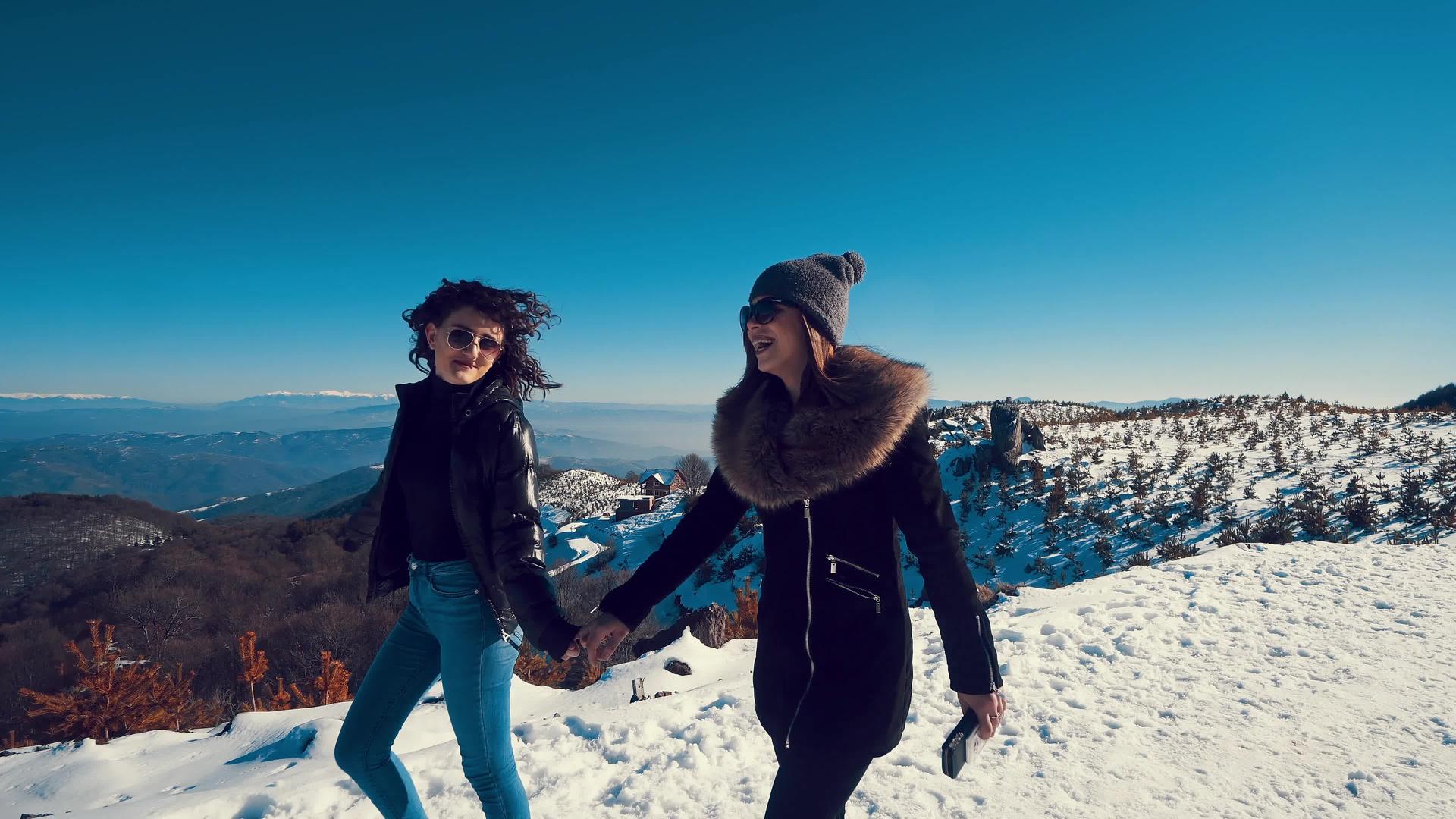 迷人美丽的女孩在雪地里走来走去手牵着手在背景中微笑视频的预览图