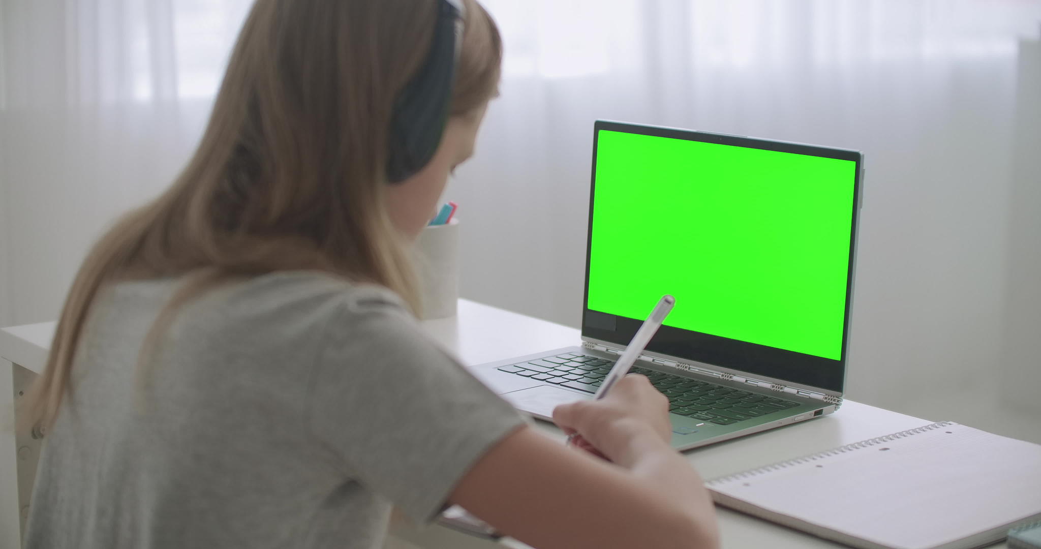 青少年女孩在网上学习坐在笔记本电脑前的桌子上手里拿着视频的预览图