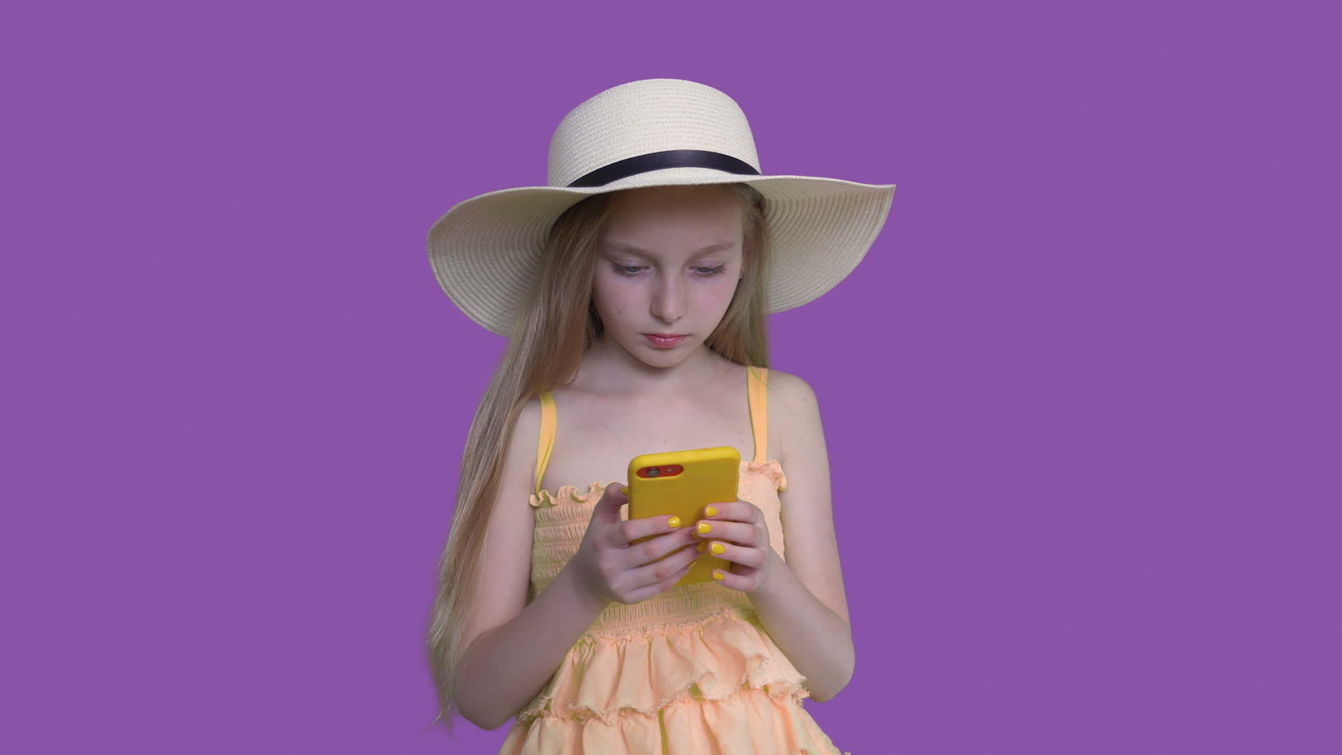 穿着夏季帽子的金发女孩使用紫色墙壁背景浏览智能手机视频的预览图