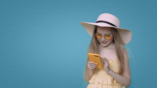 微笑着穿着黄色衣服的女孩在蓝色背景上浏览智能手机视频的预览图