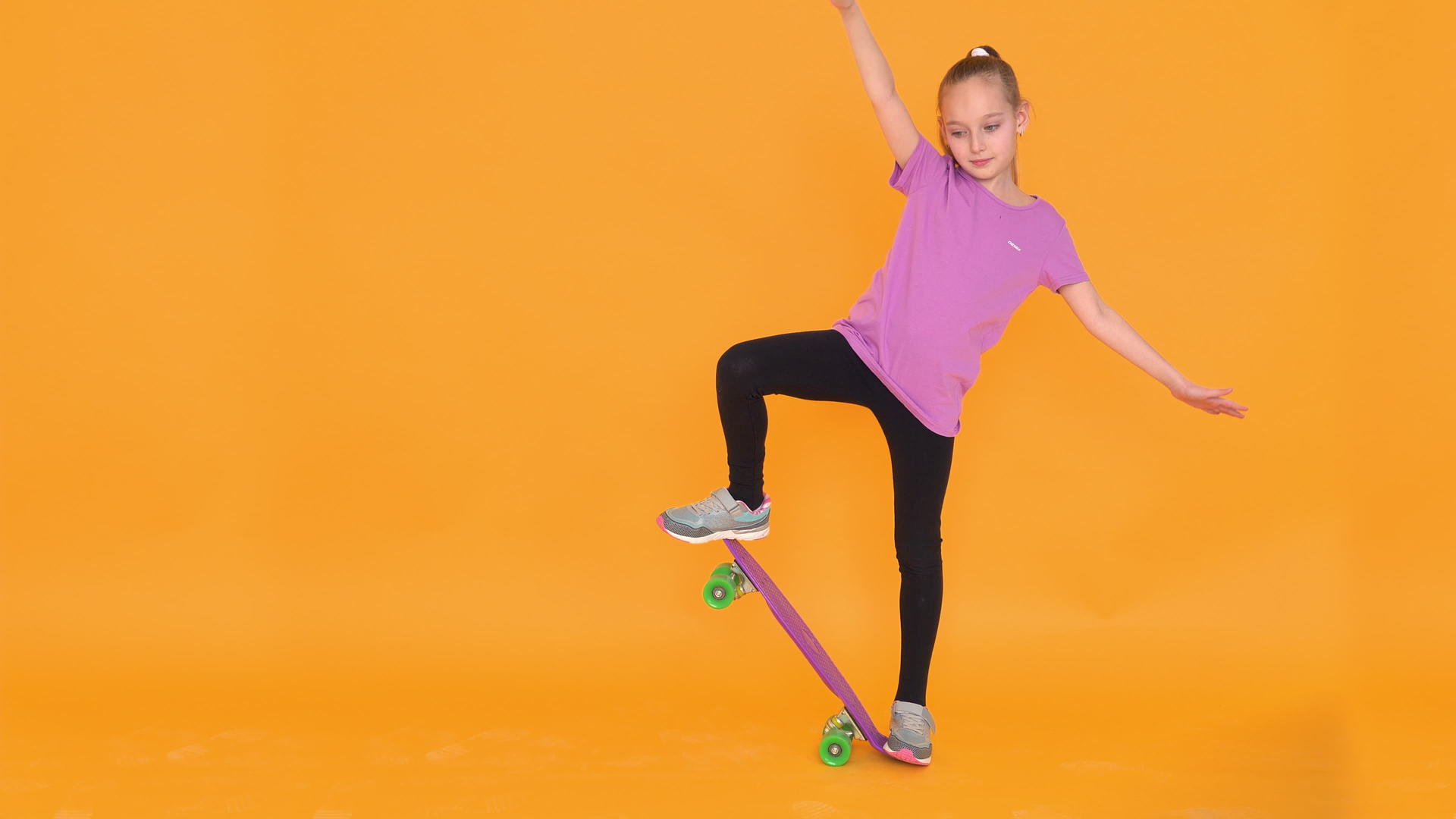以橙色背景为背景的年轻女孩在橙色背景工作室滑板上平衡视频的预览图