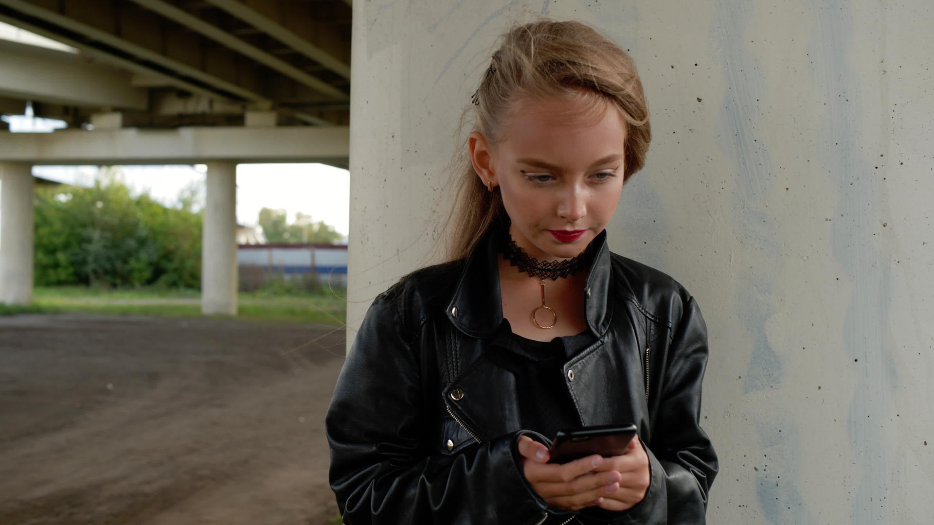 年轻女孩穿着黑色皮夹克在城市街道上使用手机视频的预览图