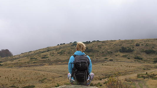 穿着蓝色夹克的女性徒步旅行者背着背包坐在岩石上视频的预览图
