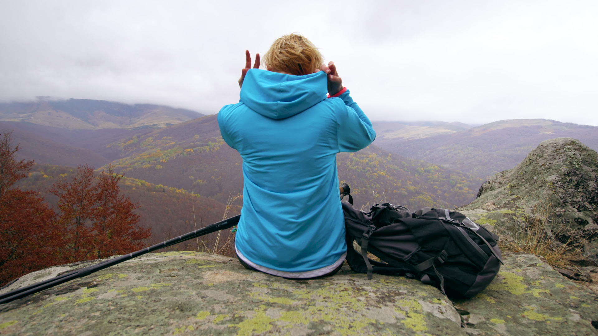 蓝色的女徒步旅行者在山上的岩石上休息移动她的兜帽视频的预览图