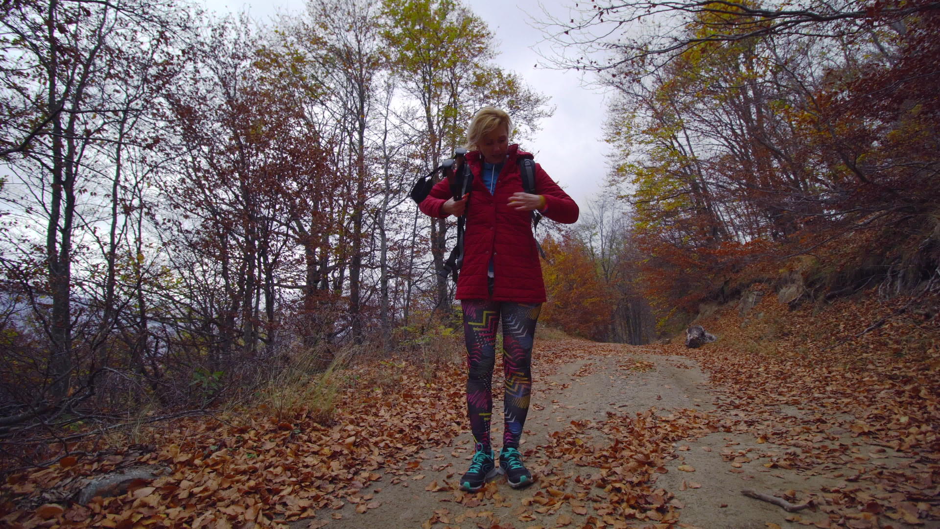 一个穿着红色夹克和背包在泥路或小路上徒步旅行的女孩视频的预览图