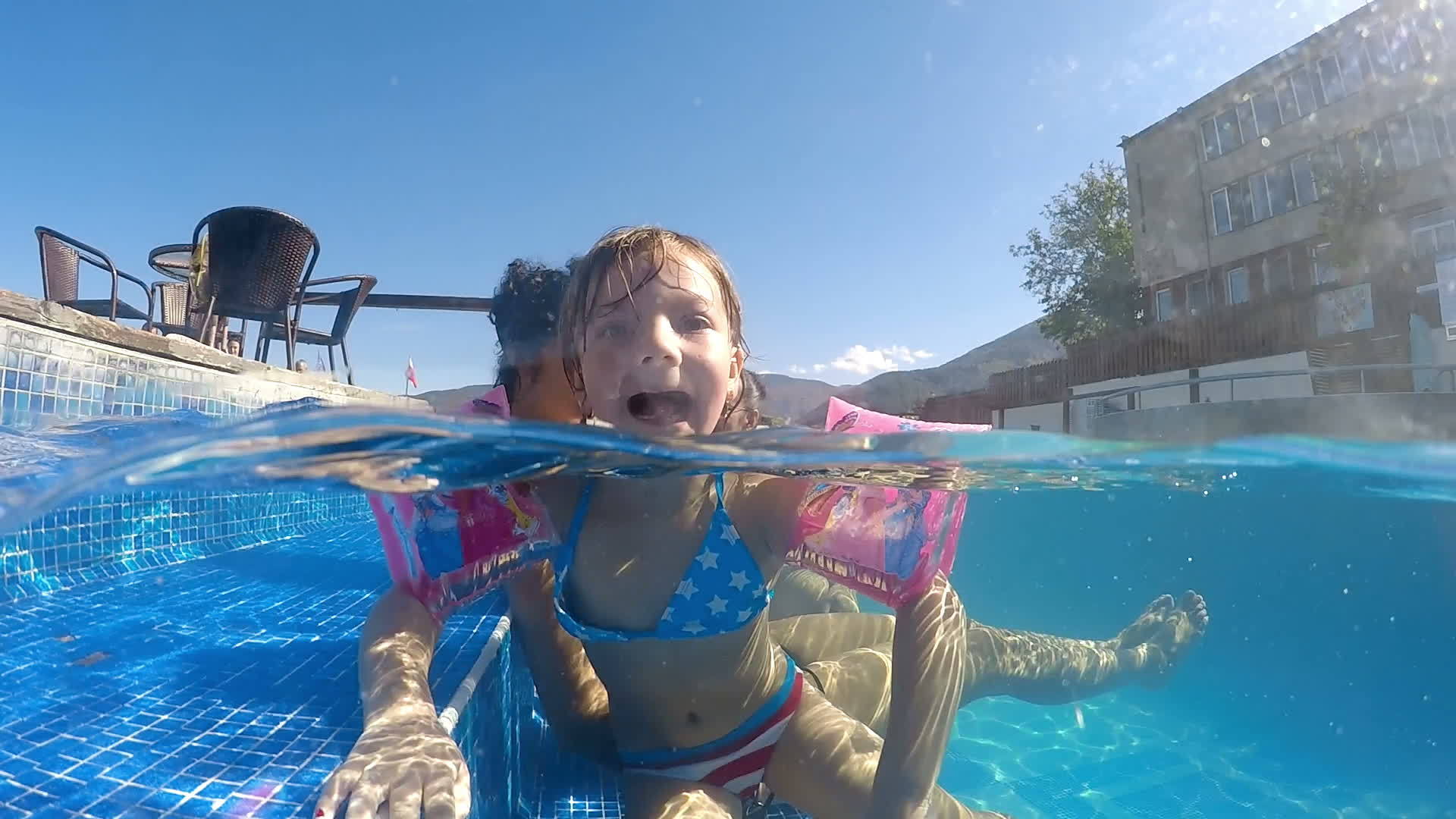 带着臂带的小女孩在游泳池里使滑稽的舌头向相机发出尖锐的声音视频的预览图